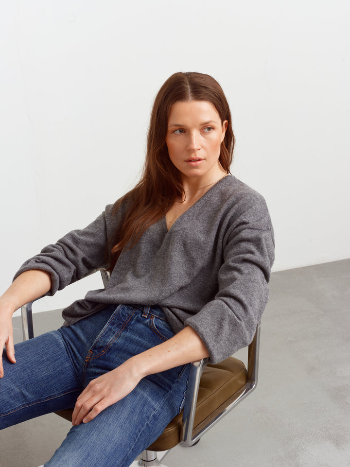 Terni sweater in mineral grey cashmere, seated with sleeves pushed up over blue jeans