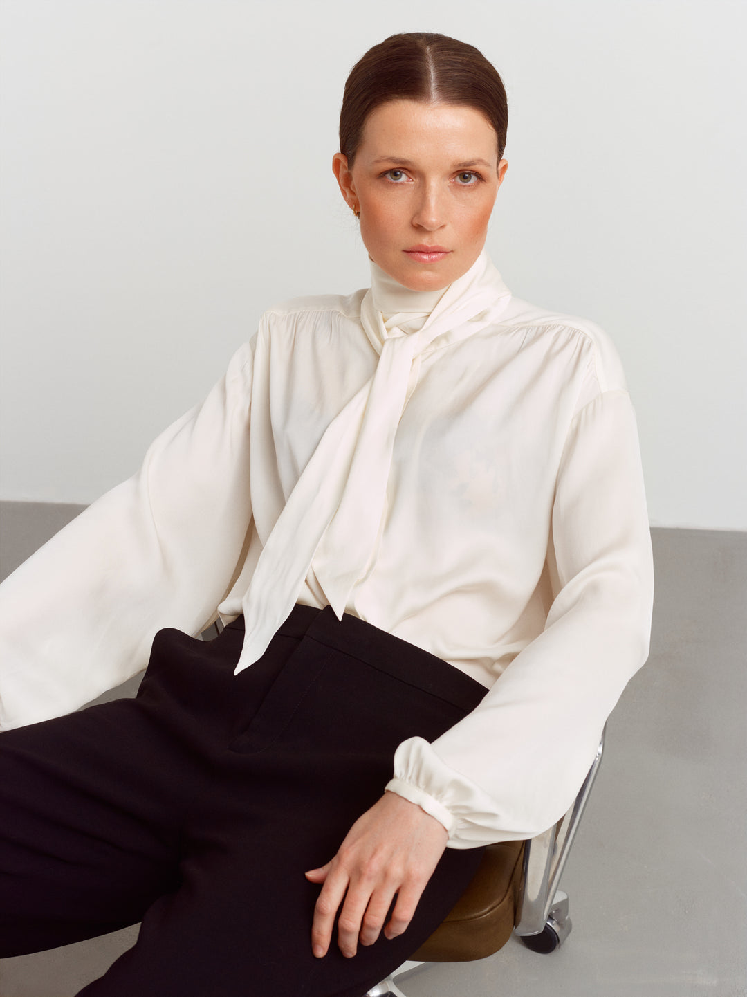 Caen blouse in cloud dancer silk blend, seated with the scarf tied at the neck over black trousers