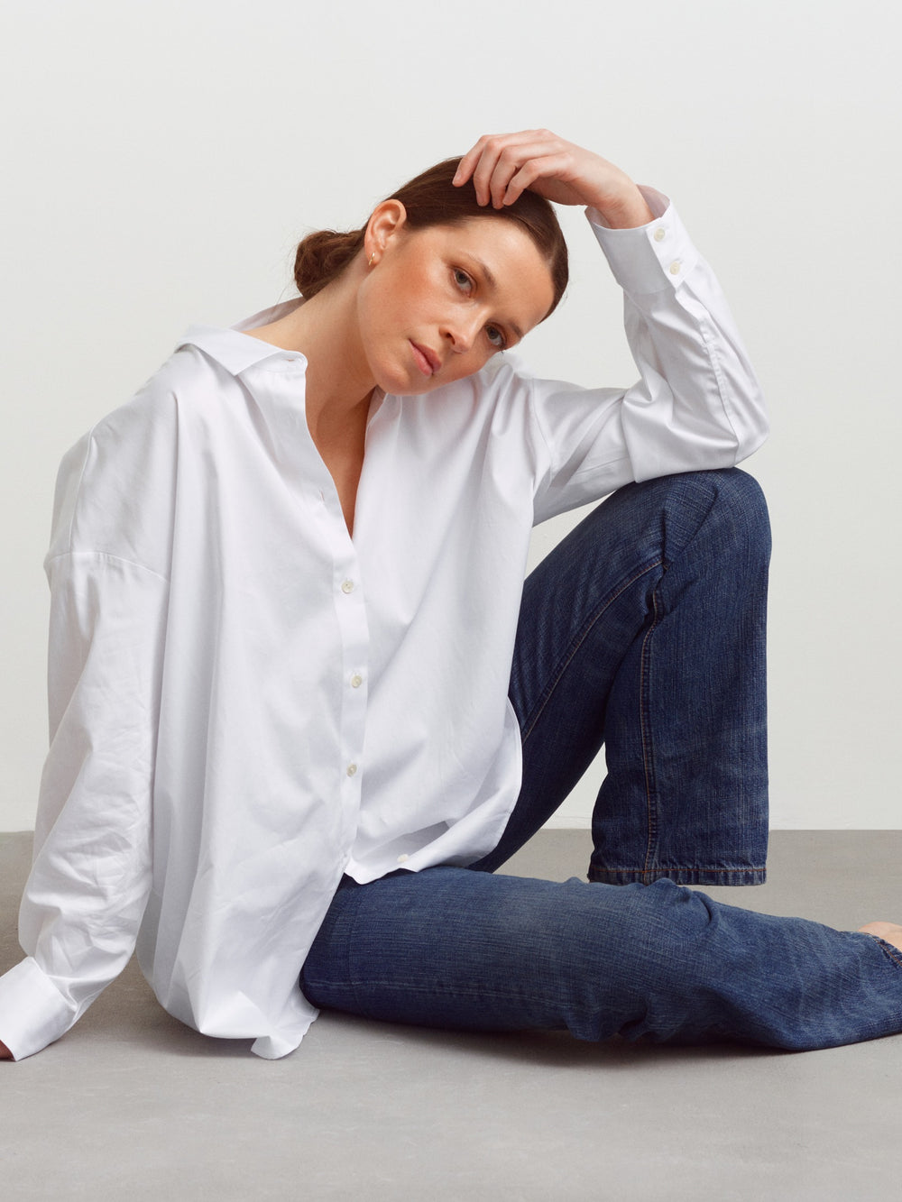 Model seated in the Copenhagen shirt in white cotton, worn with blue jeans