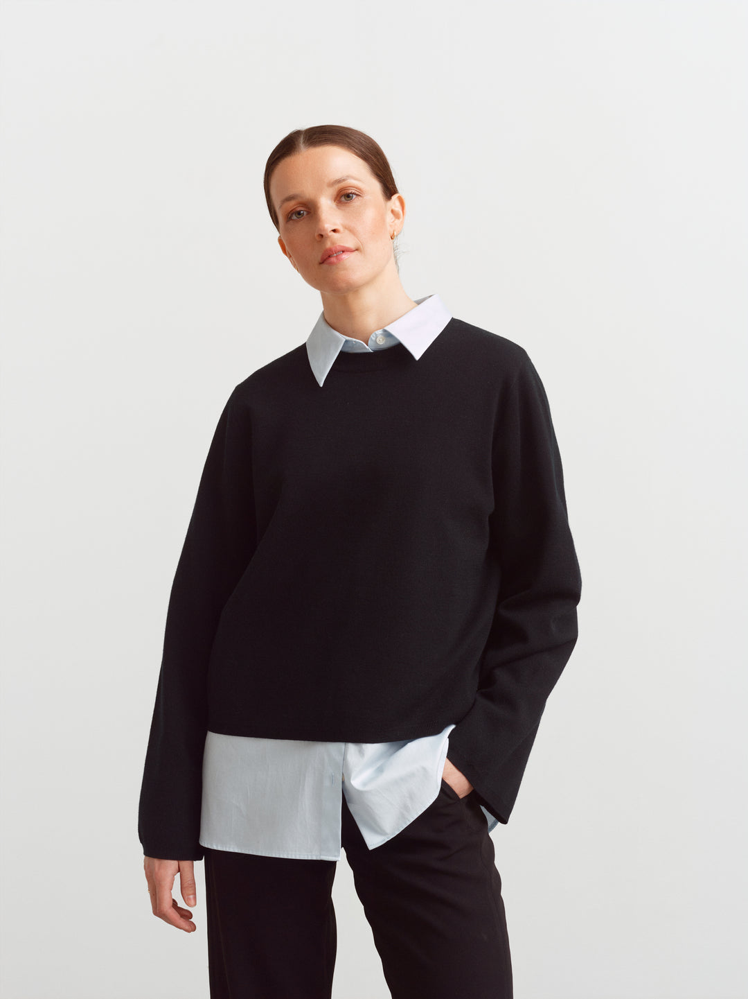 Montreal sweater in black merino wool, front view with elongated sleeves over a collared shirt