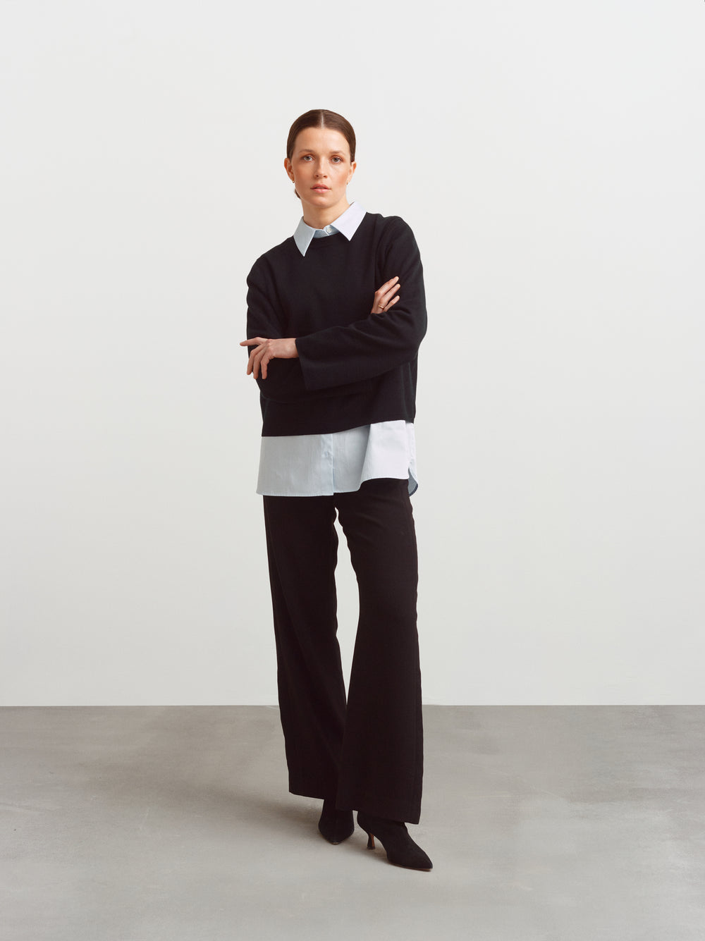 Montreal sweater in black merino wool, layered over a light blue shirt with black trousers