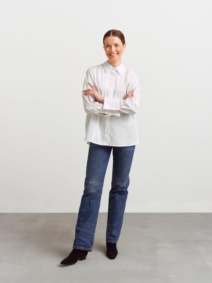 Odense shirt in white organic cotton, full figure smiling with sleeves folded back over jeans